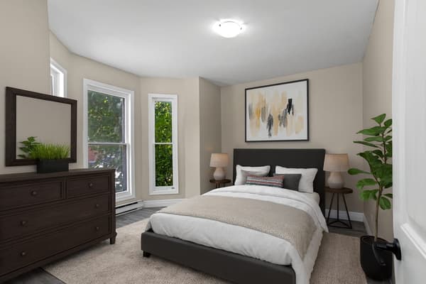 Bay window bedroom with a bed, dresser and mirror at 203 Colborne Street, Kingston, shown virtually staged